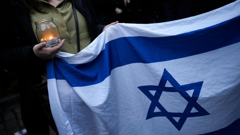 Eine Frau hält eine Kerze und eine israelische Flagge, während sie an einer Mahnwache vor einer Synagoge in Berlin, Deutschland, teilnimmt, Freitag, 13. Oktober 2023. Hunderte Berlinerinnen und Berliner versammelten sich am Vorabend des Schabbat vor der Synagoge am Fraenkelufer, um sie und den darin stattfindenden Gebetsgottesdienst vor möglichen Anschlägen zu schützen.