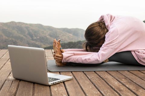 Frau übt Vorbeuge auf einer Yoga-Matte vor einem Laptop
