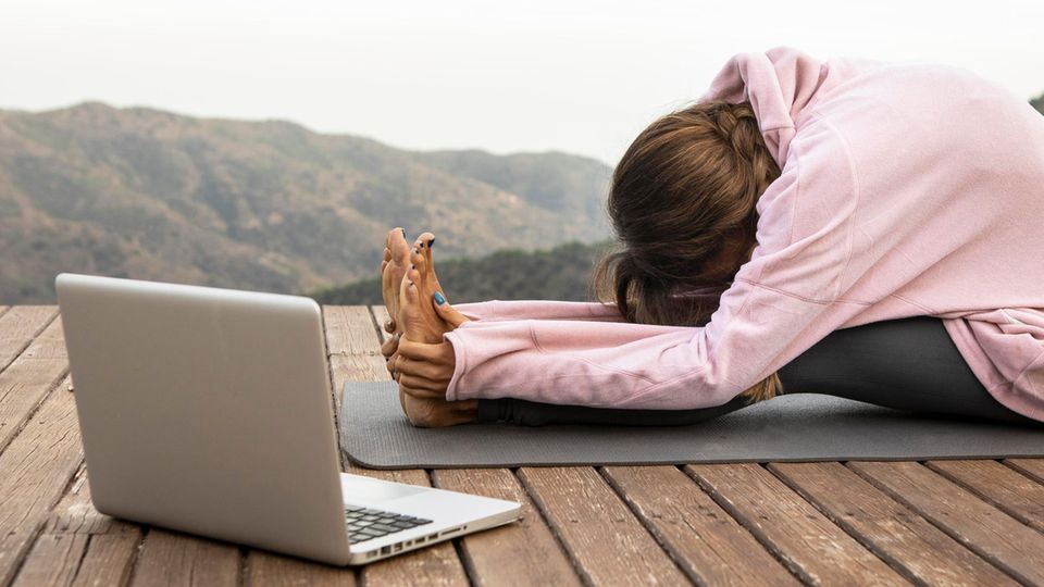 Frau übt Vorbeuge auf einer Yoga-Matte vor einem Laptop