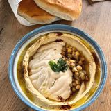 Hummus Kanaan  Oz und Jalil: Hummus kann als Dip zu unzähligen Gerichten serviert werden, auch als Brotaufstrich oder einfach zu Gemüsesticks ist er ein leckerer Snack.      Für 6 Personen  Zutaten:  300 g getrocknete Kichererbsen, 1⁄4 TL Natron, 50 ml eiskaltes Wasser, 1 TL Salz, 140 g Tahini, Saft von 1 großen Zitrone, 1⁄2 TL Zucker, Olivenöl zum Garnieren  Zubereitung:  » Die Kichererbsen über Nacht in Wasser einweichen. Am nächsten Tag in ein Sieb abgießen, gut abspülen und mit reichlich kaltem Wasser und Natron in einen großen Topf geben und aufkochen, dann ca. 1,5 Stunden kochen lassen. Sie sollten so weich sein, dass sie sich leicht zwischen zwei Fingern zerdrücken lassen.  » Den dabei entstehenden Schaum und die sich an der Oberfläche absetzenden Kichererbsenschalen mit einem großen Servierlöffel oder Schaumlöffel abschöpfen.  » In ein Sieb abgießen und das Kochwasser auffangen. Die gekochten Kichererbsen unter fließendem Wasser abspülen, um Natronreste zu entfernen.  » Die Kichererbsen in eine Küchenmaschine geben und das eiskalte Wasser zufügen. So lange pürieren, bis eine glatte, cremige Textur entstanden ist. Bei Bedarf zusätzlich etwas Kochwasser zugeben.  » Die restlichen Zutaten zufügen und weiterpürieren, bis die gewünschte Konsistenz erreicht ist. Weiteres Kochwasser zufügen, falls nötig.  » In eine Servierschale geben und mit etwas Olivenöl beträufeln. Am besten warm oder direkt nach dem Abkühlen genießen.