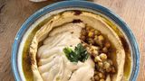 Hummus Kanaan  Oz und Jalil: Hummus kann als Dip zu unzähligen Gerichten serviert werden, auch als Brotaufstrich oder einfach zu Gemüsesticks ist er ein leckerer Snack.      Für 6 Personen  Zutaten:  300 g getrocknete Kichererbsen, 1⁄4 TL Natron, 50 ml eiskaltes Wasser, 1 TL Salz, 140 g Tahini, Saft von 1 großen Zitrone, 1⁄2 TL Zucker, Olivenöl zum Garnieren  Zubereitung:  » Die Kichererbsen über Nacht in Wasser einweichen. Am nächsten Tag in ein Sieb abgießen, gut abspülen und mit reichlich kaltem Wasser und Natron in einen großen Topf geben und aufkochen, dann ca. 1,5 Stunden kochen lassen. Sie sollten so weich sein, dass sie sich leicht zwischen zwei Fingern zerdrücken lassen.  » Den dabei entstehenden Schaum und die sich an der Oberfläche absetzenden Kichererbsenschalen mit einem großen Servierlöffel oder Schaumlöffel abschöpfen.  » In ein Sieb abgießen und das Kochwasser auffangen. Die gekochten Kichererbsen unter fließendem Wasser abspülen, um Natronreste zu entfernen.  » Die Kichererbsen in eine Küchenmaschine geben und das eiskalte Wasser zufügen. So lange pürieren, bis eine glatte, cremige Textur entstanden ist. Bei Bedarf zusätzlich etwas Kochwasser zugeben.  » Die restlichen Zutaten zufügen und weiterpürieren, bis die gewünschte Konsistenz erreicht ist. Weiteres Kochwasser zufügen, falls nötig.  » In eine Servierschale geben und mit etwas Olivenöl beträufeln. Am besten warm oder direkt nach dem Abkühlen genießen.