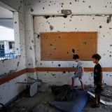 Zwei Kinder stehen in einem Klassenzimmer einer von der UN betriebenen Schule im Flüchtlingscamp Al Maghazi im Gazastreifen. Die Wände sind von Schrapnell-Einschlägen gezeichnet.