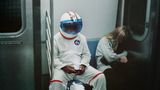 Ein an Halloween als Astronaut verkleideter Mann sitzt neben einem sich versteckenden Mädchen in der U-Bahn in NewYork