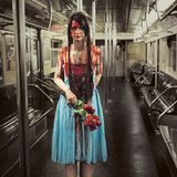 Eine zu Halloween verkleidete Frau im Kostüm "Carrie" Blutverschmiert mit blauem Kleid, Krönchen und einem Strauß Rosen