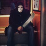 Ein Mann mit Maske und einem großen unechten Messer sitzt als Swordsman verkleidet an Halloween in einer New Yorker U-Bahn