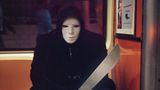 Ein Mann mit Maske und einem großen unechten Messer sitzt als Swordsman verkleidet an Halloween in einer New Yorker U-Bahn