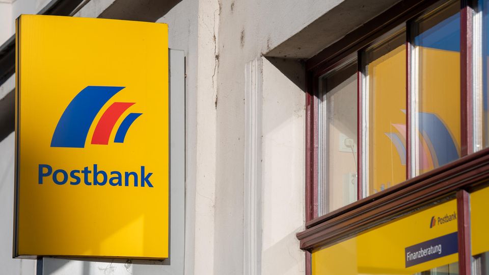 Ein Schild mit dem Logo der Postbank ist an der Fassade einer Bankfiliale angebracht