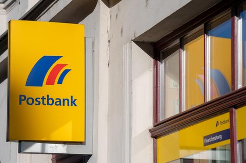 Ein Schild mit dem Logo der Postbank ist an der Fassade einer Bankfiliale angebracht