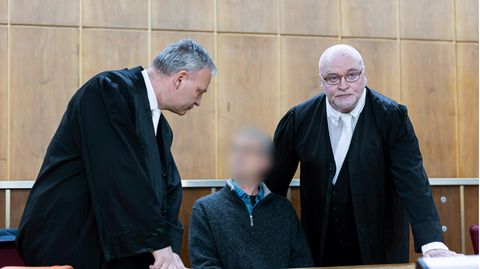 Der Angeklagte sitzt vor Verhandlungsbeginn in einem Gerichtssaal im Landgericht Hannover. Daneben stehen seine Anwälte
