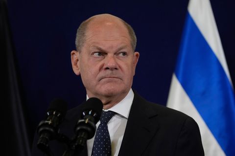 Olaf Scholz schaut ernst. Er steht vor einer israelischen Fahne bei seinem Besuch in Tel Aviv