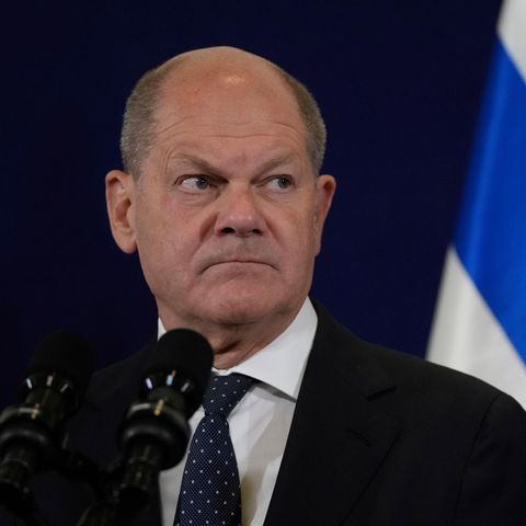 Olaf Scholz schaut ernst. Er steht vor einer israelischen Fahne bei seinem Besuch in Tel Aviv