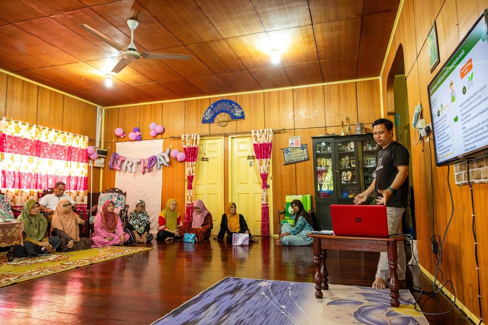 Menschen sitzen in einem Raum auf dem Boden und beobachten einen Vortrag