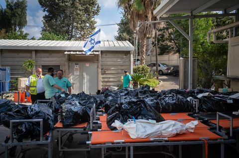 Zahlreiche Leichensäcke liegen aufgereiht vor einer Israel-Flagge