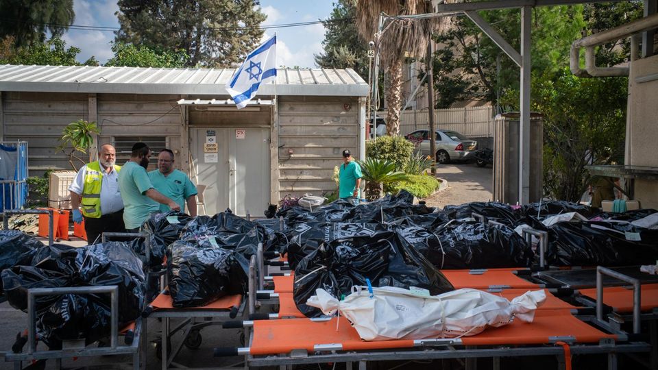Zahlreiche Leichensäcke liegen aufgereiht vor einer Israel-Flagge