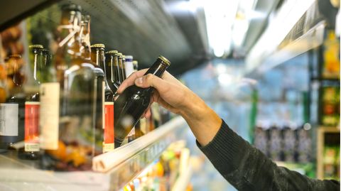 Ein Mann in einem Supermarkt nimmt eine Bierflasche aus dem Regal