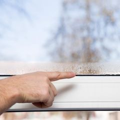 Person zeigt auf Fenster, das durch zu hohe Luftfeuchtigkeit beschlagen ist