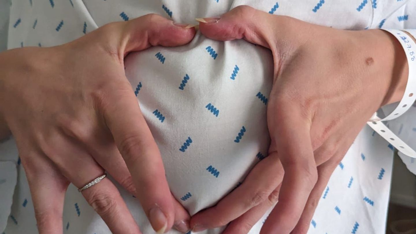 Zwei Hände formen ein Herz um eine Brust im OP-Kittel