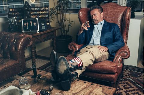 Portrait von Arnold Schwarzenegger mit Cowboystiefeln und Zigarre im Ledersessel