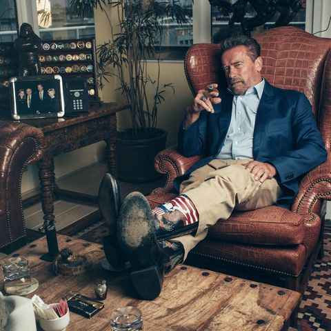 Portrait von Arnold Schwarzenegger mit Cowboystiefeln und Zigarre im Ledersessel