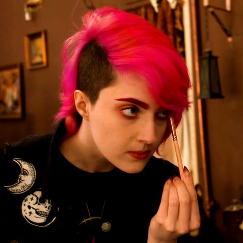 Die moderne Hexe Shisha Rainbow schminkt sich vor einem Spiegel