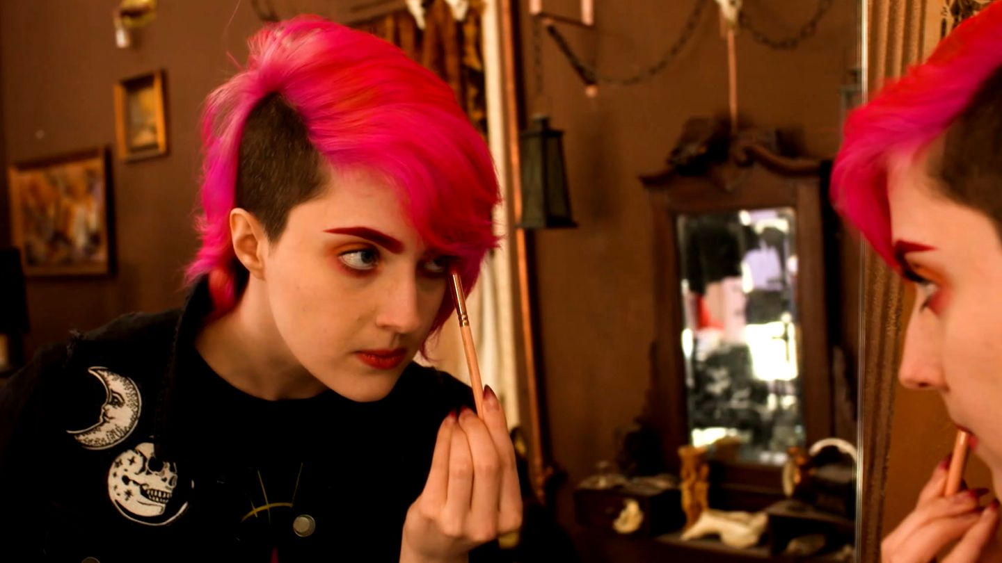Die moderne Hexe Shisha Rainbow schminkt sich vor einem Spiegel