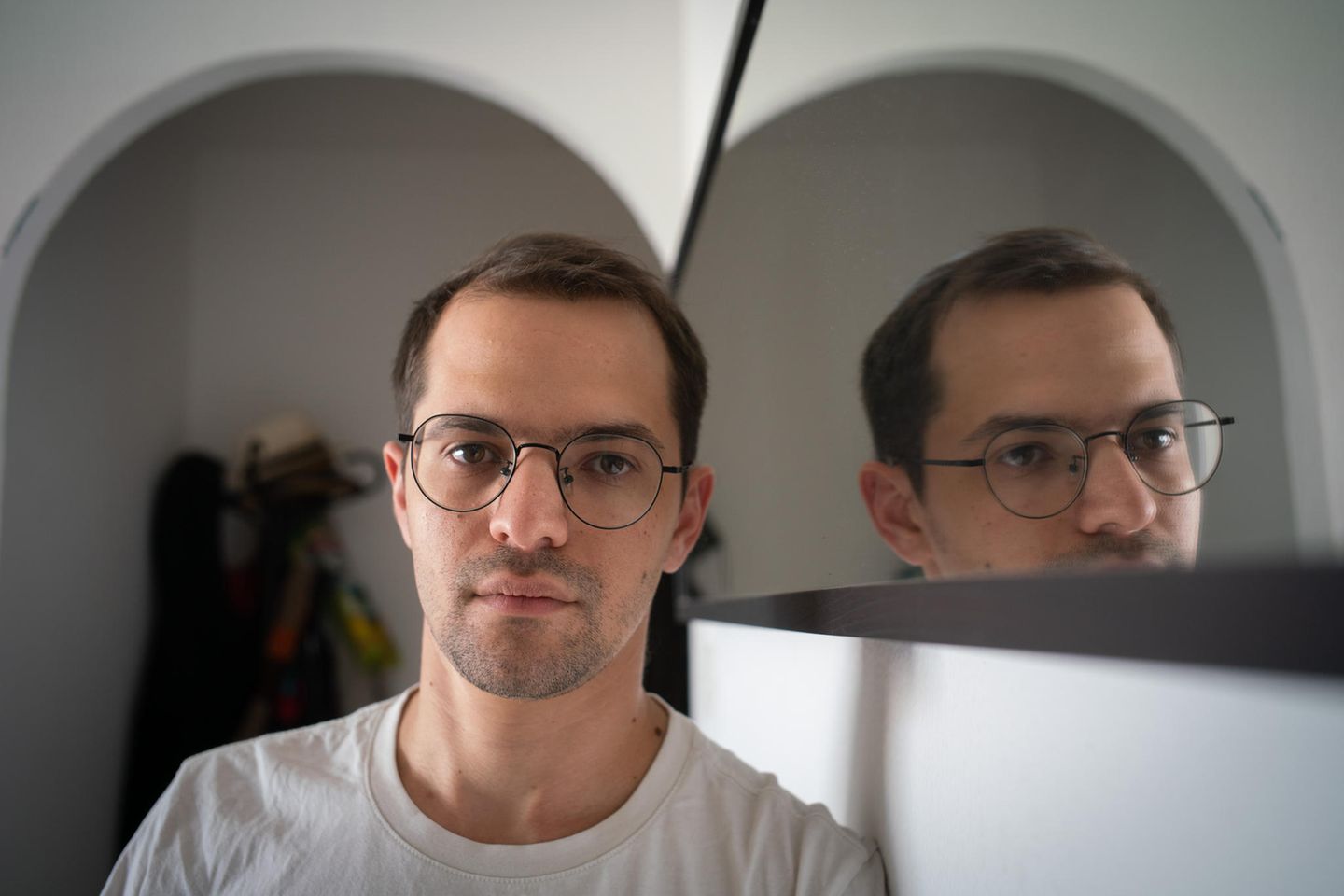 Kampf von Haus zu Haus Benzion Sanders, braune kurze Haare mit Brille und weißem T-shirt, neben einem Spiegel