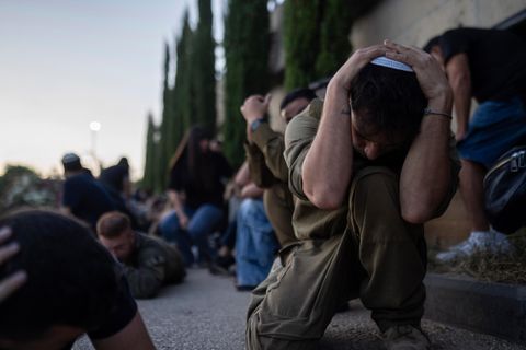 Eine Gruppe Menschen kauert schutzsuchend auf dem Boden.