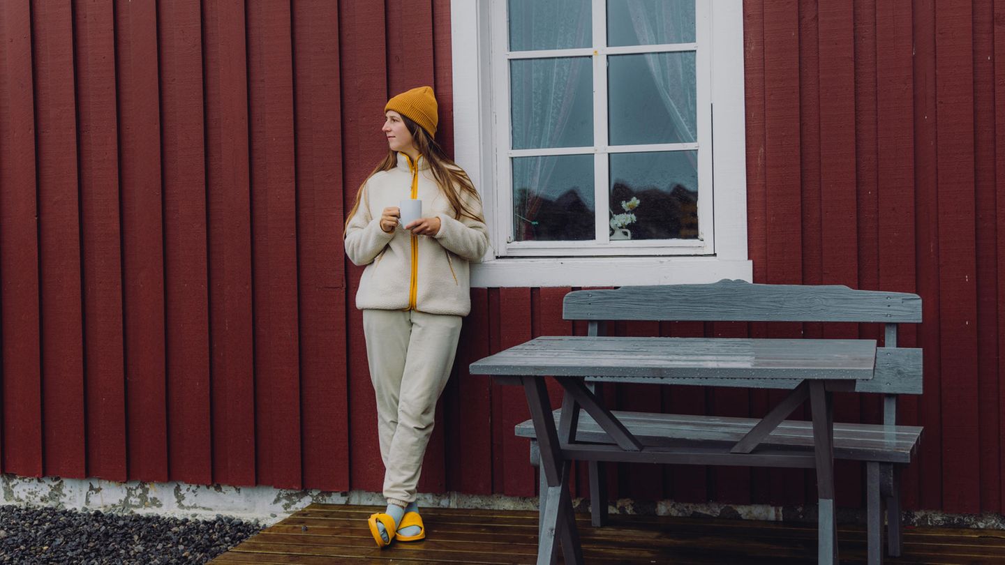 Reisende, die eine morgendliche Tasse Kaffee von rotem Rorbu auf den Lofoten genießt