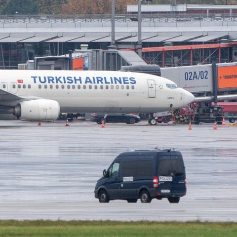 Ein Polizeifahrzeug steht auf dem Flughafen vor einem Flugzeug, an dem ein Auto mit einem Geiselnehmer steht