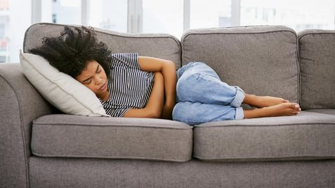 Frau liegt mit Bauchkrämpfen auf dem Sofa