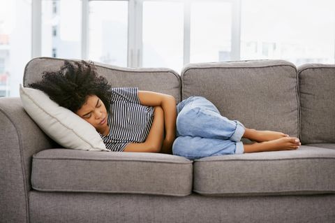 Frau liegt mit Bauchkrämpfen auf dem Sofa
