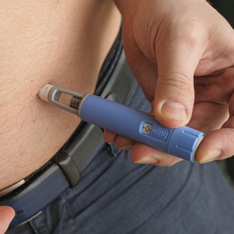 A man wearing dark trousers places the light blue Ozempic injection pen on his bare stomach