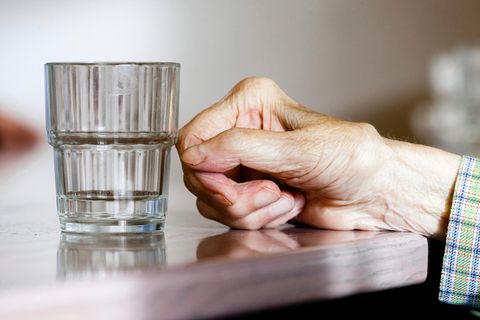 Die Hand einer alten Frau mit Demenz neben einem Wasserglas