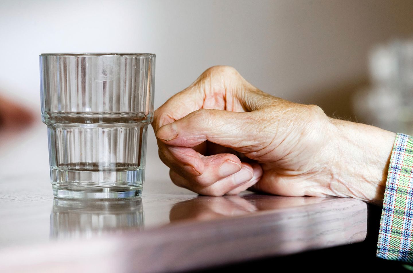 Die Hand einer alten Frau mit Demenz neben einem Wasserglas