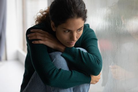 Frau sitzt traurig vor dem Fenster und hat Weltschmerz