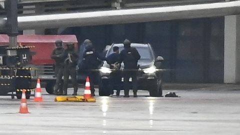 Polizei in Kampfmontur umstellt ein Auto am Flughafen Hamburg, vor dem ein Mann in Handschellen steht