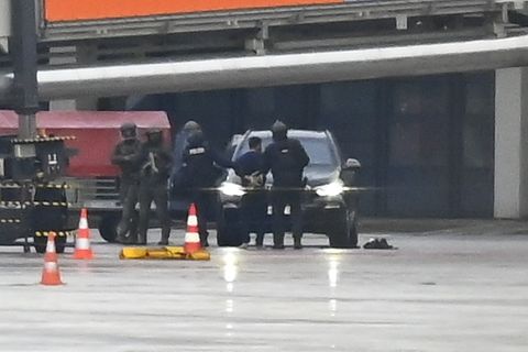 Polizei in Kampfmontur umstellt ein Auto am Flughafen Hamburg, vor dem ein Mann in Handschellen steht
