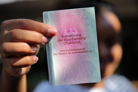 Eine Frau mit afrikanischen Wurzeln hält eine Duldung in die Kamera