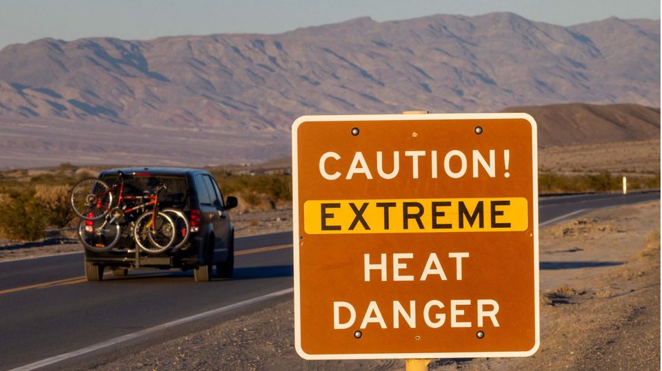 Ein Auto fährt an einem Schild im Death Valley National Park vorbei, das vor extremer Hitze warnt