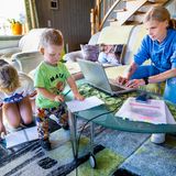 Frau arbeitet am Laptop, daneben zwei kleine Kinder