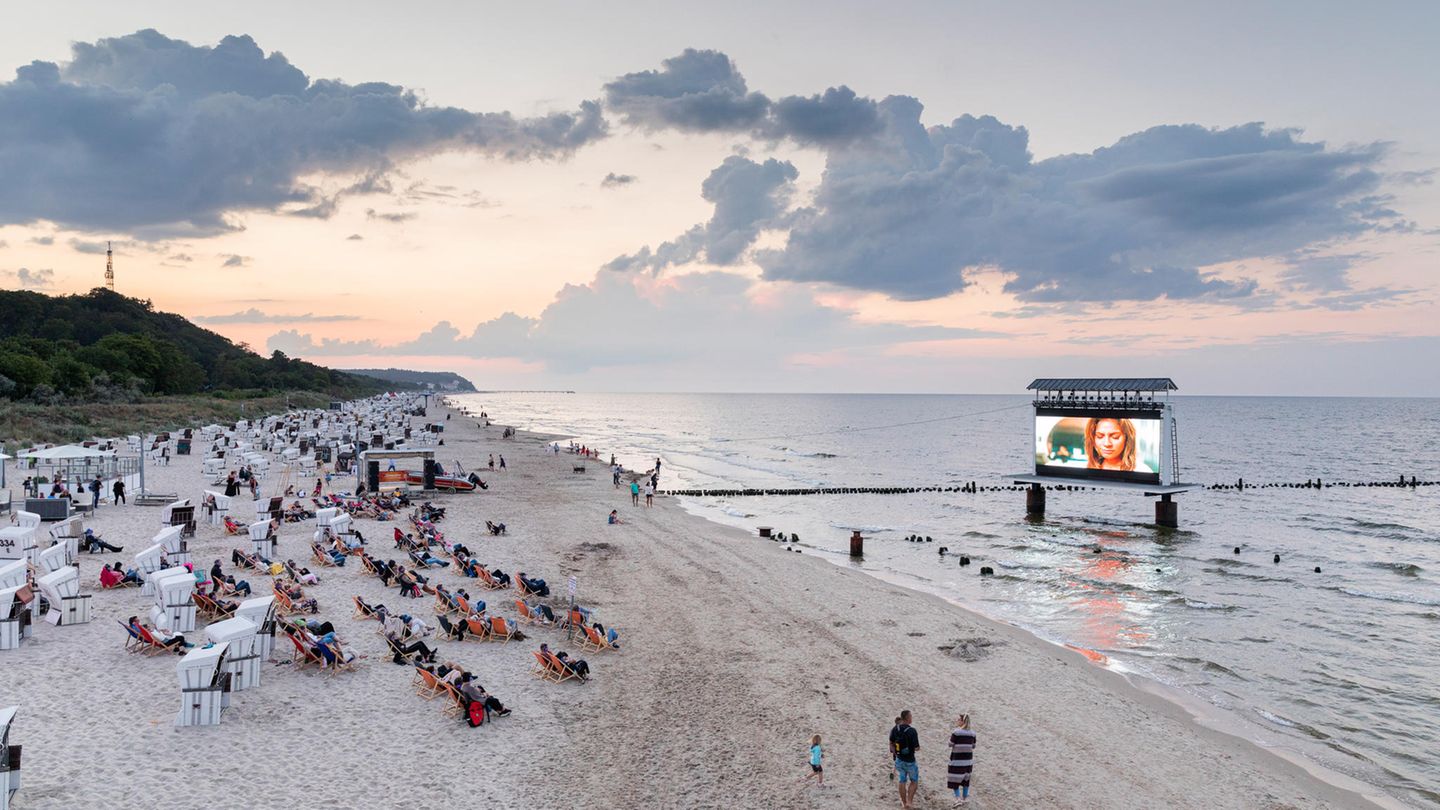 Menschen in Liegestühlen am Strand gucken Kinofilm