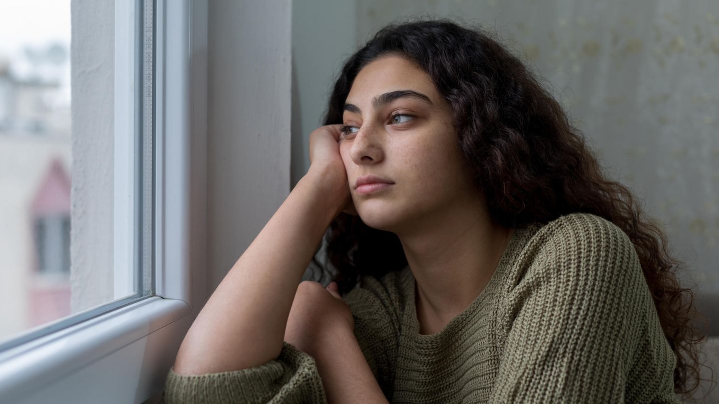 Eine junge Frau mit langen dunklen Haaren blickt sehnsüchtig aus dem Fenster