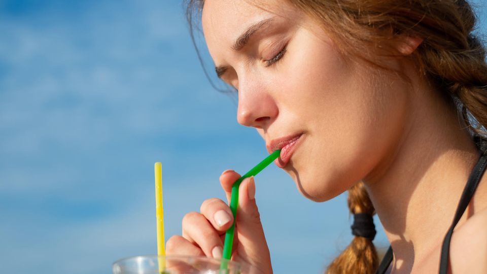 Eine junge Frau trinkt aus einem Plastikstrohhalm
