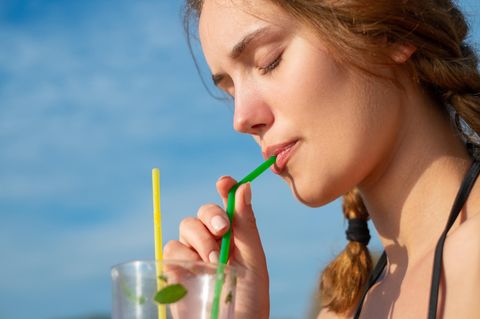 Eine junge Frau trinkt aus einem Plastikstrohhalm
