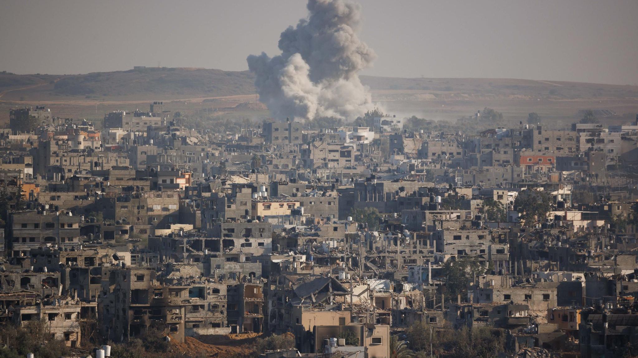 Eine Ansicht von einer vollkommen zerstörten Gegend in Gaza-Stadt, am Horizont eine Rauchwolke einer Explosion