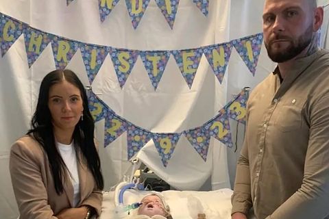 Eine Frau und ein Mann stehen neben einem Kinderbett, in dem ein Baby mit Schläuchen in der Nase liegt