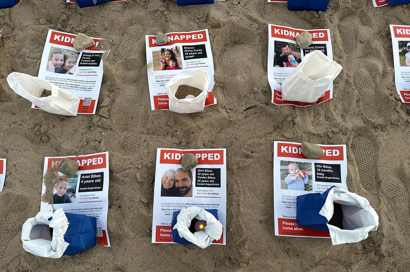 Flugblätter machen auf verschleppte angehörige aufmerksam, sie liegen im Sand, auf Ihnen stehen Kerzen