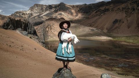 Eine Frau steht mit einem Alpaka auf dem Arm in den peruanischen Anden