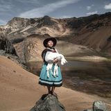 Eine Frau steht mit einem Alpaka auf dem Arm in den peruanischen Anden