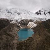 Ein blauer Gletschersee neben braunen Flächen, dahinter Eis